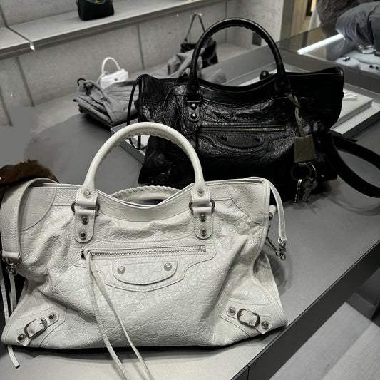 Large capacity AriaLuxe studded biker shoulder bag in white, displayed alongside a black version on a sleek surface.