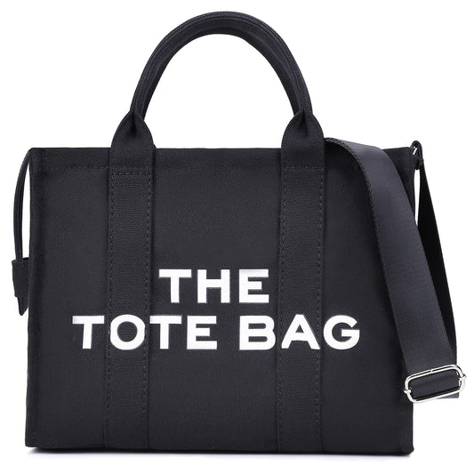 Black tote bag with white text reading "THE TOTE BAG," featuring sturdy handles and an adjustable shoulder strap.